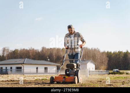 Giovane che utilizza una macchina per aerazione per scarificare e aerare prati o prati Foto Stock