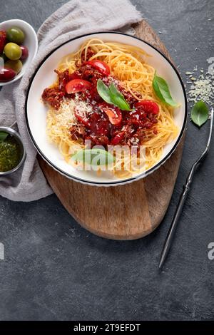 Gustosi e appetitosi spaghetti italiani classici, pasta alla bolognese con salsa di pomodoro, parmigiano di formaggio, carne e basilico su piatto su sfondo scuro. Vista dall'alto. Foto Stock