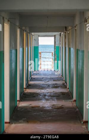 Corridoio con porte in un edificio abbandonato durante il giorno e vista mare. Foto Stock