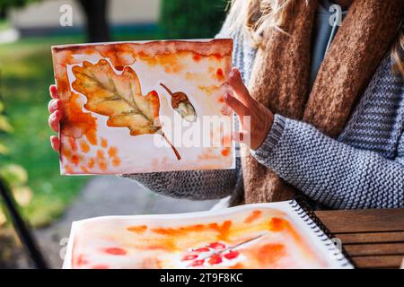 Artista donna mostra il suo acquerello con un tema autunnale. Hobby artistico creativo Foto Stock