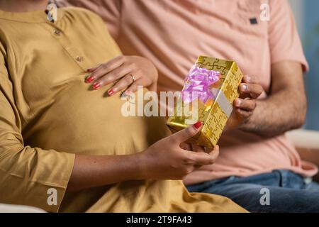 Primo piano del marito indiano che regala una moglie incinta a casa - concetto di maternità, regalo di anniversario e celebrazione della maternità Foto Stock