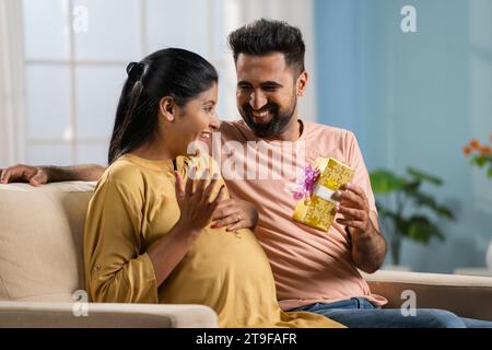 felice marito indiano che regala una moglie incinta abbracciando a casa - concetto di relazione romantica, affetto e stile di vita maternità. Foto Stock