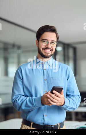 Felice giovane uomo d'affari latino con smartphone in ufficio. Verticale. Foto Stock