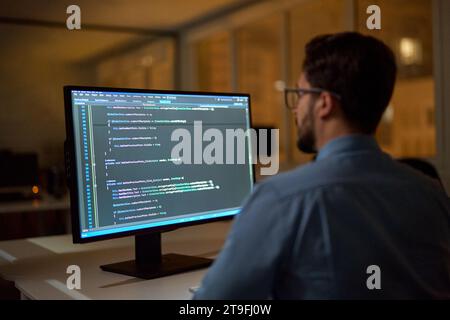 Un uomo d'affari impegnato sviluppatore di software che lavora su un computer pc in ufficio di notte. Foto Stock