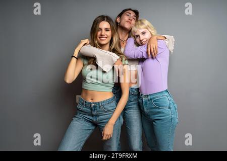 Tre donne diverse che si abbracciano e sorridono in un ambiente da studio, rappresentando calore, amicizia e connessione gioiosa. Foto Stock