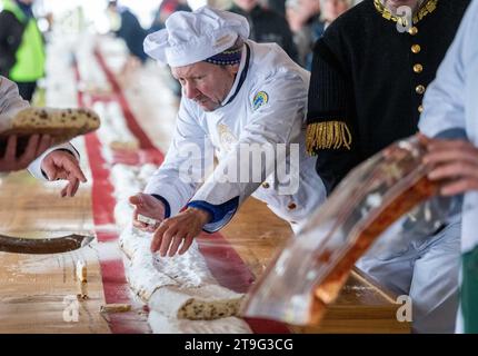 Dorfchemnitz, Germania. 25 novembre 2023. Una sosta natalizia lunga 40 metri viene tagliata al 1° festival Saxon Stollen nel villaggio avventura forestale di Blockhausen. Lo stollen era composto da singoli pezzi forniti da 25 panetterie di tre gilde (Erzgebirge, Vogtland e Meißen). I pezzi di sgabello sono stati venduti per una buona causa. Crediti: Kristin Schmidt/dpa/Alamy Live News Foto Stock