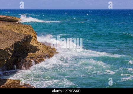 Le onde blu del Mar dei Caraibi si schiantano contro le coste rocciose dell'isola di Aruba. Foto Stock