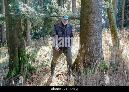 Un uomo sorridente cammina attraverso la soleggiata foresta autunnale circondata da erba dorata. Paesaggi naturali unici e un'atmosfera autunnale rilassata. Foto Stock