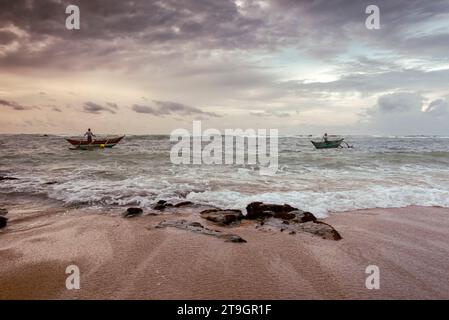 Due pescatori in piccole barche cercano di prendere un giorno di pesca la mattina presto vicino a Mirissa, in Sri Lanka Foto Stock