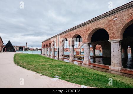 Venezia, Italia - 9 novembre 2023: Arsenale veneziano con portici, canale ed erba verde in un giorno di pioggia Foto Stock