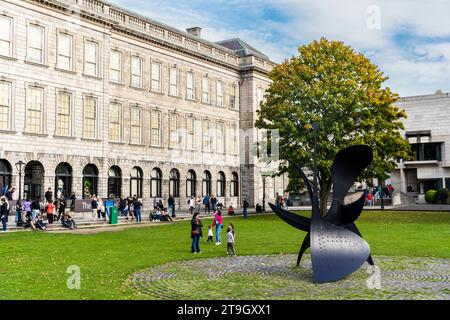 Fellow's Square con una scultura moderna di fronte alla Old Library, campus del Trinity College, centro di Dublino, Irlanda, con i turisti in un sunn Foto Stock