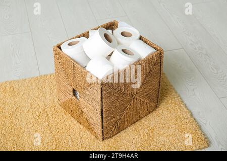 Cestino in vimini con rotoli di carta igienica sul pavimento Foto Stock