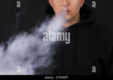 Uomo irriconoscibile nella nuvola di fumo di vape. Tizio che fuma sigaretta elettronica per smettere di fumare tabacco. Concetto di fumo senza nicotina alternativa e vapore, copia spac Foto Stock