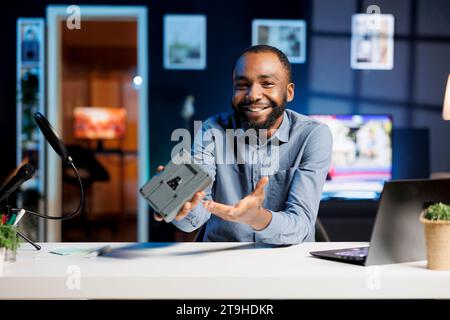 Tech Influencer disimballaggio e revisione di una batteria con montaggio a V ad alta capacità utilizzata per alimentare dispositivi di fascia alta. L'host online presenta una fonte di alimentazione portatile ricaricabile al litio da casa studio Foto Stock