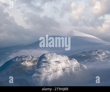 Neve coperta montagne invernali in ultima sera luce del sole. Magnifico crepuscolo ventoso sulle cime sopra la pittoresca località sciistica alpina Foto Stock