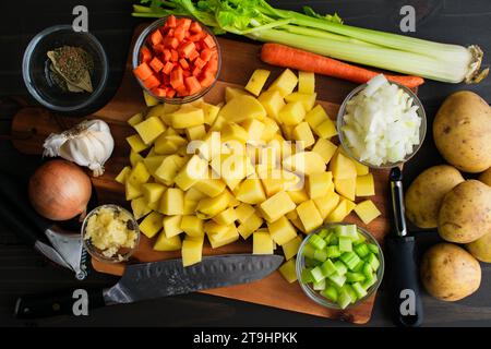 Patate gialle tritate circondate da altri ingredienti: Patate preparate, carote, cipolle, sedano e aglio con utensili da cucina Foto Stock
