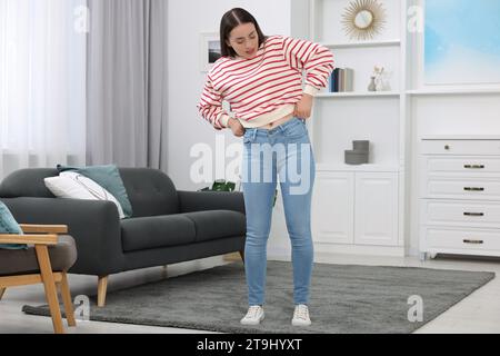 Donna che cerca di indossare jeans stretti a casa Foto Stock