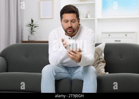 Uomo che emette un bacio durante la video chat tramite smartphone a casa. Relazione a distanza Foto Stock
