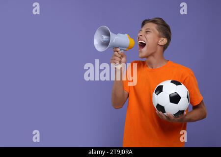 Fan dello sport con la palla da calcio che urla in megafono su sfondo viola. Spazio per il testo Foto Stock