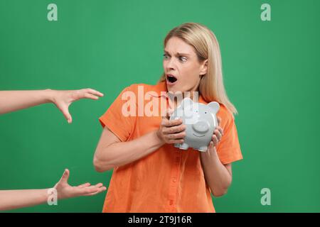 Truffatore che prende salvadanaio da una donna emotiva su sfondo verde. Attenzione - frode Foto Stock