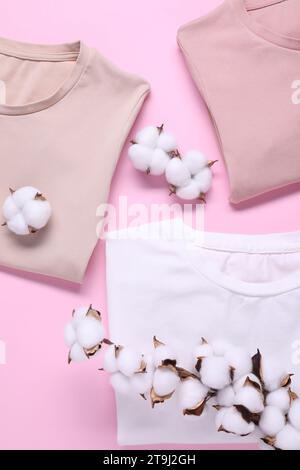 Rametto di cotone con fiori soffici e t-shirt su sfondo rosa, piatto Foto Stock