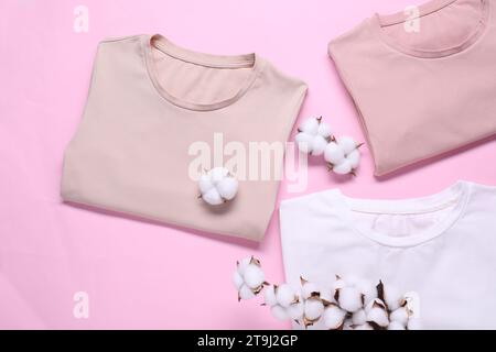 Rametto di cotone con fiori soffici e t-shirt su sfondo rosa, piatto Foto Stock