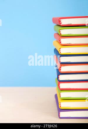 Primo piano su libri rilegati colorati e luminosi impilati su un tavolo di legno chiaro con sfondo blu. Metà dei libri in mostra. Minimalismo. Foto Stock