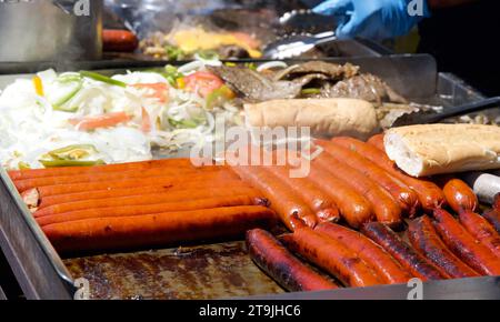 Primo piano su piatti alla griglia all'aperto con hot dog freschi, salsicce, cipolle e bistecche per sandwich. Popolare fair food. Foto Stock