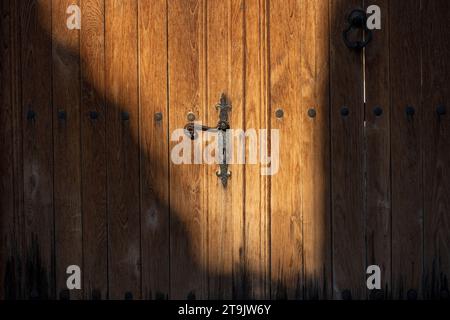 Vecchia porta marrone in legno illuminata dal sole. Luce e ombra. Maniglia della portiera in metallo. Foto Stock