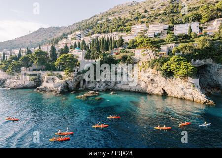 Un gruppo di kayak colorati galleggia sul mare lungo una costa rocciosa. Drone Foto Stock