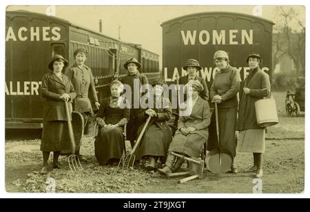 Cartolina originale dell'era della prima guerra mondiale di donne che reclutano lavoratori terrestri/carrozze ferroviarie per le sistemazioni, Northallerton e lavoratori del terreno scritta su pullman. La donna in abiti civili davanti, che indossa un vestito, è probabilmente un organizzatore di reclutamento, un ufficiale o un allenatore. Si pensa che si tratti di una fotografia pubblicitaria per il reclutamento, in quanto le donne sono in possesso di una selezione di strumenti come forche, rastrello, una falda e lattina di latte e sgabello per mungere. Forse le donne sono state in un corso di addestramento militare terrestre. Al contrario è scritto "1st set of landworkers Feb 26th to March 26th 1917" Northallerton, North Yorkshire, Regno Unito Foto Stock