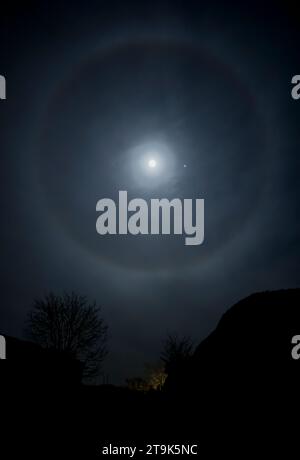 Un alone solare si forma intorno alla luna piena in una fredda notte di novembre, Worcestershire, Inghilterra. Il pianeta Giove può essere visto a destra della luna. Foto Stock