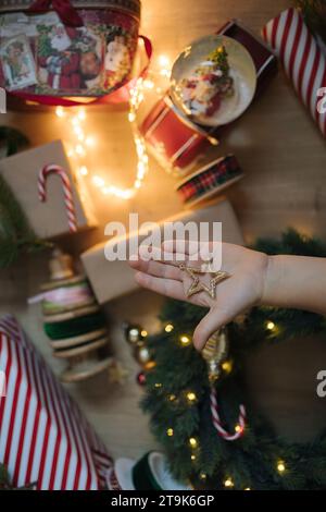 Una bambina tiene in mano una stella d'oro giocattolo nel palmo dello sfondo delle luci e delle decorazioni natalizie Foto Stock