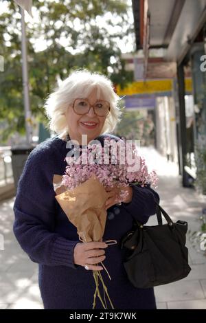 anziana donna anziana sorridente con bouquet di fiori per strada Foto Stock