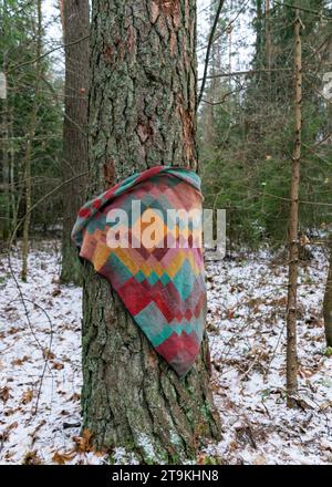 sciarpa a maglia e calda avvolta intorno ad un tronco d'albero, sciarpa colorata lavorata a mano in stile entralact, maglia di lana, inverno Foto Stock