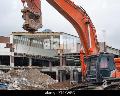 Demolizione di un edificio del centro commerciale con una grande macchina da escavatore. Distruggere una vecchia casa per fare spazio a un nuovo cantiere. Cumuli di sporcizia Foto Stock