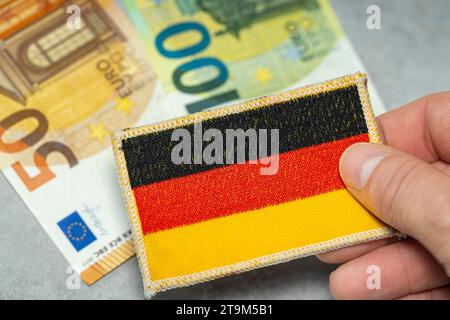 Moneta in euro in Germania, situazione finanziaria ed economica della Germania, bandiera tedesca tenuta in mano su un sfondo di banconote da 50 e 100 euro Foto Stock