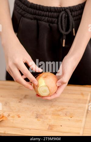 Le mani femminili sfoggiano un'intera cipolla su uno sfondo rustico in legno, mettendo in risalto la freschezza e il fascino terroso di questo capo indispensabile per la cucina Foto Stock