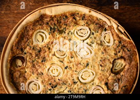 Creazione saporita: Una torta di porri e uova ben sfornata, disposta su un tavolo di legno, affascina con il suo fascino saporito Foto Stock