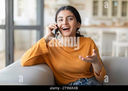 Chiamata piacevole. Felice giovane donna indiana che parla al cellulare a casa Foto Stock