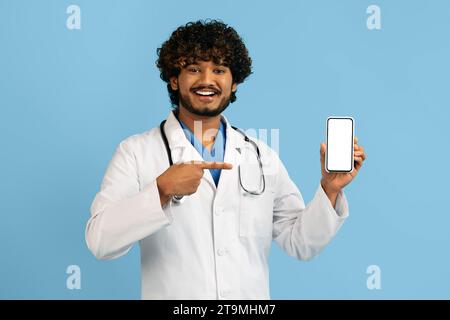 Bello allegro medico indiano che mostra smartphone con schermo vuoto Foto Stock