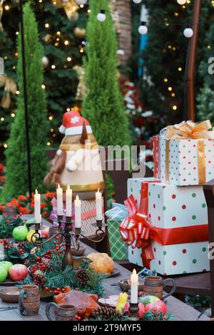 Un ambiente all'aperto festoso con un tavolo di Natale decorato circondato da alberi sullo sfondo Foto Stock