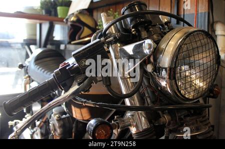 Immagine ravvicinata di una motocicletta parcheggiata in un garage poco illuminato, circondata da oggetti vari Foto Stock