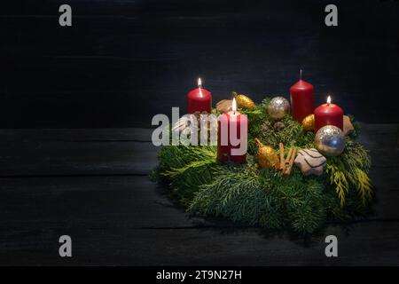 Luce al buio al terzo avvento, corona verde naturale con candele rosse, tre sono in fiamme, decorazione natalizia e biscotti, fondo di legno scuro, Foto Stock