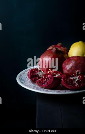 Pezzi di melograno freschi e succosi in piatto di porcellana bianca su un tavolo di legno nero. Frutta fresca su sfondo scuro. Foto Stock