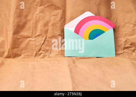 Busta verde con una carta a forma di arcobaleno su sfondo testurizzato di cartone. Foto Stock