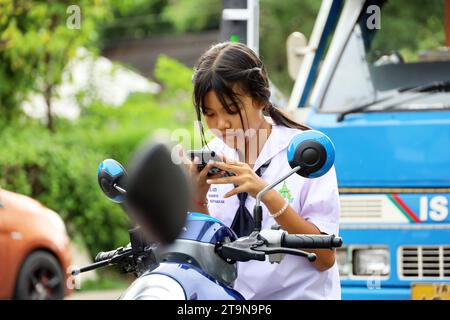 Ragazza thailandese che usa lo smartphone mentre si guida in moto per strada Foto Stock