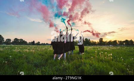 Gli studenti si laureano con fumo colorato che cammina attraverso il prato la sera. Foto Stock