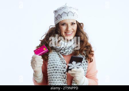 Ciao inverno. donna moderna felice con maglione, guanti, cappello e sciarpa con fiocco di neve, smartphone e carta di credito che fa shopping online su e-commerce si Foto Stock