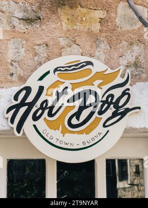 Budva, Montenegro - 08 agosto 2023: Cartello rotondo per un caffè su una vecchia facciata in pietra di una casa. Didascalia: Hot dog Foto Stock